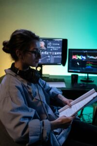 A creative professional wearing headphones reads notes in a dimly lit studio setting with computer screens.